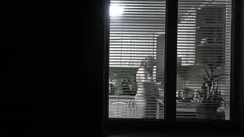 Peeping. Voyeur. Neighbor pervert voyeur in evening on street looks out window as naked sexy neighbor in kitchen prepares dinner for her husband. Naked in public. Naked at home. Family.  Outdoor